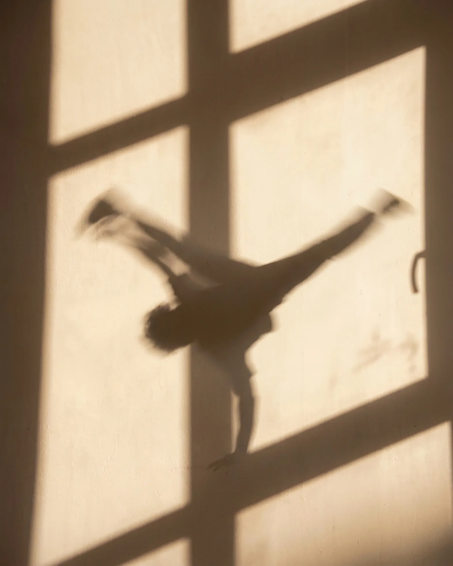 Ombre d’un danseur en équilibre sur une main, projetée sur un mur ensoleillé
